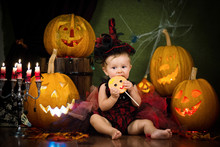 Little Witch Laughs With Candy In The Hands Among The Pumpkins And Candles.