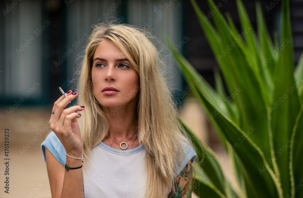 Beautiful blonde girl smokes a cigarette. Women's hands with a tattoo.  Urban fashion Stock Photo
