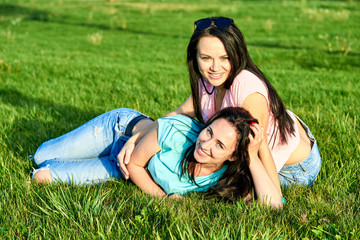 Two young happy girls lie on green grass