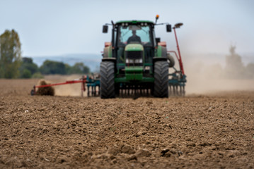 Aufkleber - Close-up of crop with Tractor ploughing field in the background. Farmer with tractor seeding.