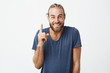 © Cookie Studio - Happy handsome bearded guy with stylish hairstyle brightful smiling with teeth and pointing upside with finger on white background. Copy space