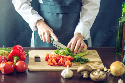 Zdjęcie XXL Szef kuchni w czarnym fartuchu tnie warzywa. Koncepcja ekologicznych produktów do gotowania
