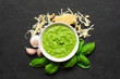 Pesto sauce in a bowl with pine nuts, parmesan and garlic over black stone background