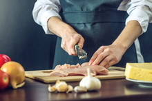 The Chef In Black Apron Cuts Chicken Fillet Knife. Concept Of Eco-friendly Products For Cooking