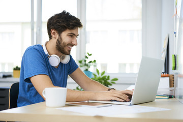 Wall Mural - Smiling student using laptop at home