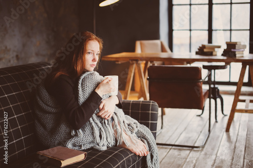 Fotografia young sick woman healing with hot drink at home on cozy couch, wrapped in knitte