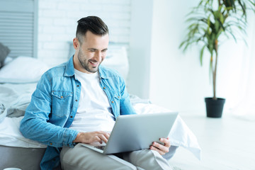 Joyful man grinning broadly while using laptop