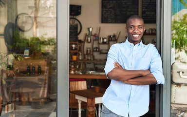 Smiling African entrepreneur standing at the door of his cafe