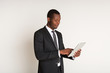 © Prostock-studio - Black male satisfied manager in suit standing, using tablet, texting. Portrait