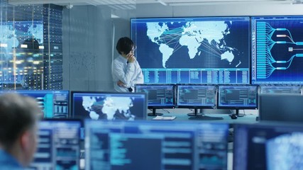 Fototapete - In the System Control Room Chief Engineer Thinks While Standing Before Big Screen with Interactive Map on it. Data Center is Full of Monitors Showing Graphics. 