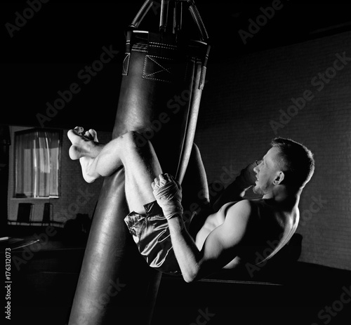 The boxer in the gym hung on a boxing bag and makes twists for the abdominal muscles Fototapete