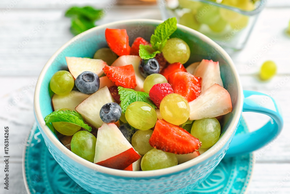 Cup with delicious fruit salad on wooden table
