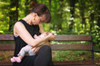 © Deymos.HR - Mother breastfeeding her newborn baby girl in the park, sitting on the bench under the trees, instagram style effect applied