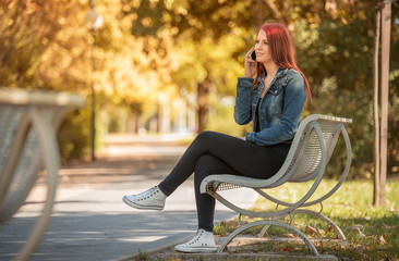 Charming woman sitting in park and call someone with phone