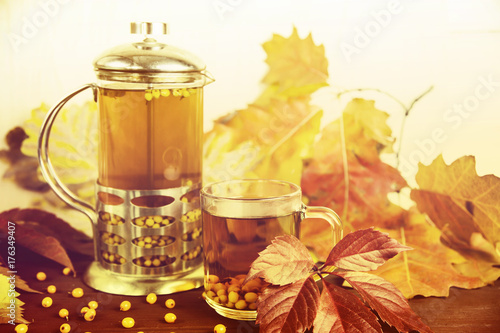 Plakat napar z herbatą z rokitnika obok przezroczystego kubka wśród jesiennych liści