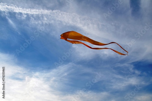 Plakat Duży latawiec w kolorze żółtym, wykonany z jedwabiu, skłania się ku niebu ku białym chmurom Cirrus