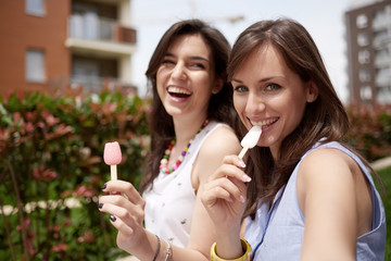 Two girls enjoying sunny day and eating ice cream outdoors