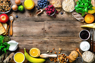 Wall Mural - Healthy breakfast ingredients, food frame. Granola, egg, nuts, fruits, berries, toast, milk, yogurt, orange juice, cheese, banana, apple on wooden rustic background, top view, copy space