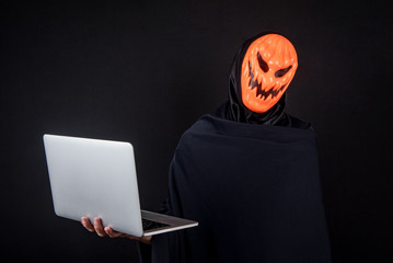 anonymous male hacker with pumpkin halloween mask carrying laptop computer. internet security and cy