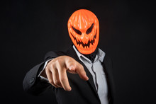Mystery Business Man With Orange Pumpkin Evil Mask And Working Suit Pointing Hand On Black Background, Halloween Night Costume Concept