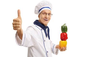 Wall Mural - Elderly chef with peppers making a thumb up gesture