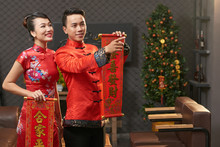 Young Vietnamese Couple Wearing Traditional Costumes Holding Scrolls With New Year Couplets In Hands While Wrapped Up In Living Room Decoration
