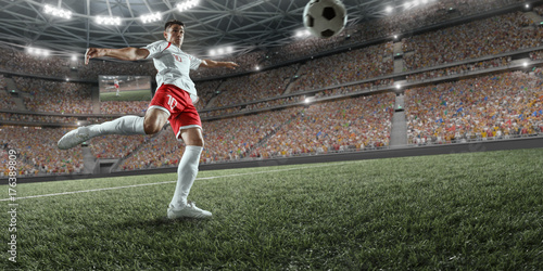 Plakat Piłkarz wykonuje grę akcji i bije piłkę na profesjonalnym stadionie. Gracz nosi niemarkowy mundur sportowy.