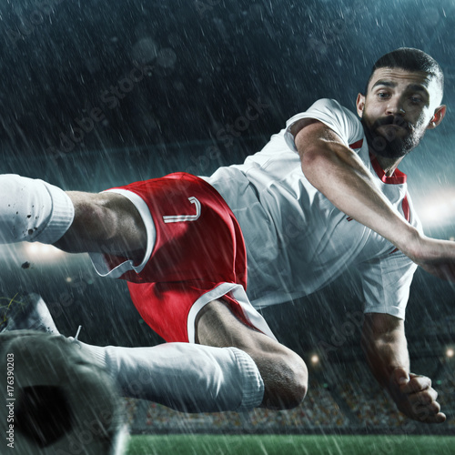 Zdjęcie XXL Piłkarz wykonuje grę akcji i bije piłkę na profesjonalnym stadionie deszczowym. Gracz nosi niemarkowy mundur sportowy.
