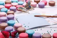 Set Of Different Colorful Macaroons Placed Over A White Wooden Background, A Postcard And A Pencil Near The Place, Space To Write.