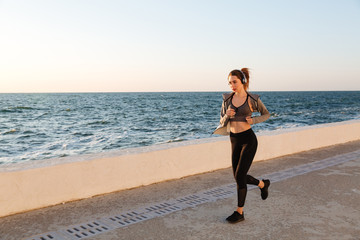 Wall Mural - Beautiful sportive woman in headphones running at the seaside