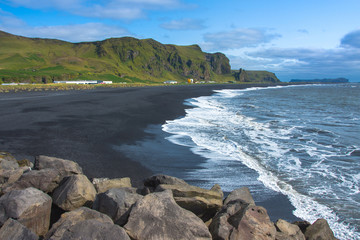 Volcanic rock on black sand beach at Vik in southern Iceland with eroded stone arch visible in distance