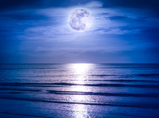 Colorful sky with dark cloud and bright full moon over seascape.