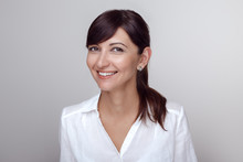 Closeup Portrait Of Beautiful Smiling Young Middle Age Brunette Caucasian Woman With Brown Eyes Looking In Camera. Girl Female With Long Dark Hair In White Office Shirt. Studio Beauty Shot.