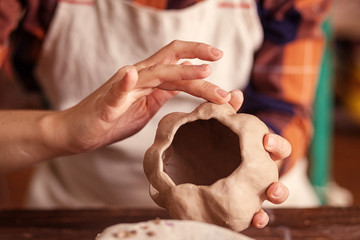 A close-up of a female potter sculpts a small pumpkin with clay jacka with a jack's face for Halloween on a wooden table background