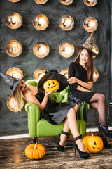 two women in halloween costumes on party sitting on chair over bulb background