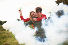 Young Couple Surrounded By Smoke From Smoke Flares In Field