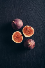 Figs on dark black slate background. Freshly cut slices of ripe fruit on rustic stone cutting board. Top view.