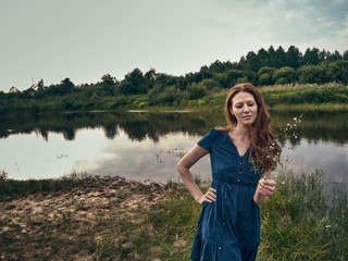 The red-haired girl in a blue summer dress strolls along the lake.