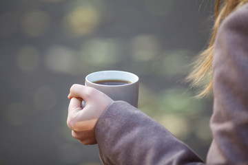 holding coffee or tea from cup in autumn park