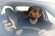 © Ovidiu - Man texting while driving.  Using a smartphone while driving.  Front view of man driving while using mobile phone.
