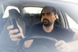 © Ovidiu - Man texting while driving.  Using a smartphone while driving.  Front view of man driving while using mobile phone.