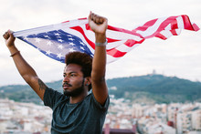 Young Black Man Waving An American Flag Outdoors.