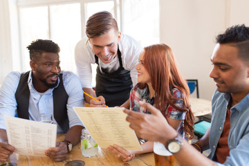 waiter and friends with menu and drinks at bar