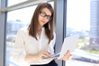 © volha_r - Modern business woman typing on laptop computer while standing in the office before meeting or presentation