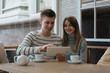 © Krystsina - Young nice couple sitting in cafe wrapped in cozy blanket drinking tea. Love story of a girl and a boy. Man and woman embrace one another on a terrace. Sweet couple choosing what to read on a tablet.