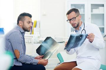 Wall Mural - Serious radiologist showing x-ray images of joints to patient and giving him consultation