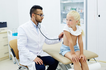 Wall Mural - Little girl sitting on couchette while physician with stethoscope examining her