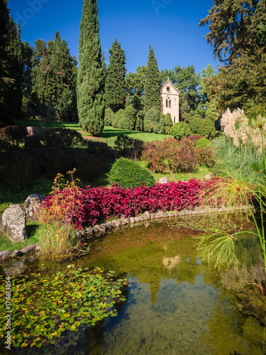 Plakat Piękny ogród z oczkiem wodnym i małym kościołem.