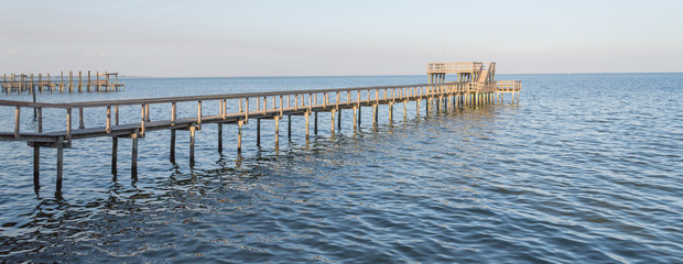 Fishing piers stretching out over Galveston Bay in Kemah, Texas, USA. Foot pier for saltwater fishing of vacation home/beach house rental/bay home in Lighthouse District waterfront at sunset. Panorama