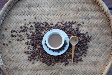 Wall Mural - A white cup of hot coffee and coffee beans put interspersed on wooden knit bamboo tray traditional north of Thailand for background,wallpaper
